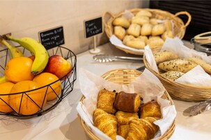 Un bufé de desayuno con canastas de cruasanes, panecillos y naranjas.
