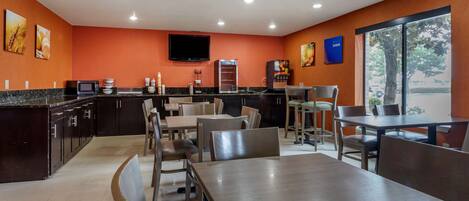 A modern restaurant with a kitchen area, dining tables, and chairs.