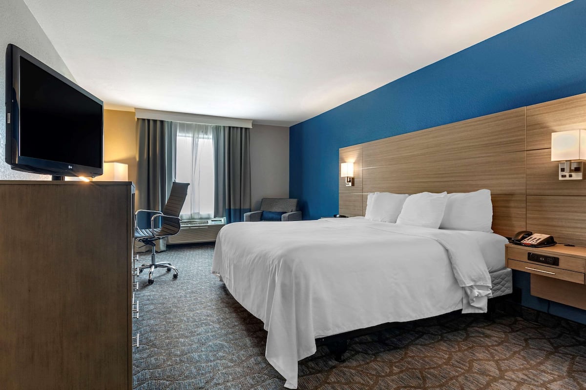 A hotel room with a large bed, a desk with a lamp, a TV, and a chair.