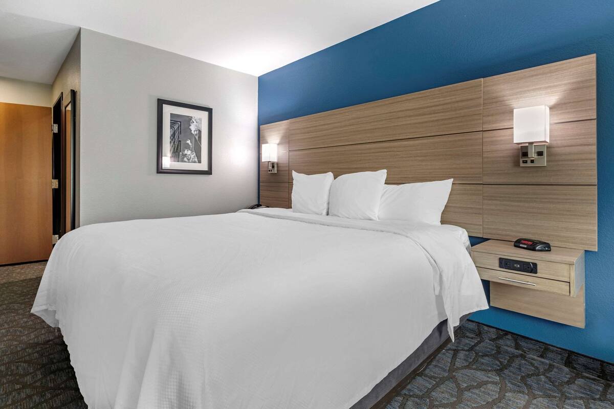 A hotel room with a large bed, a nightstand with a lamp, a framed picture on the wall, and a wooden headboard.