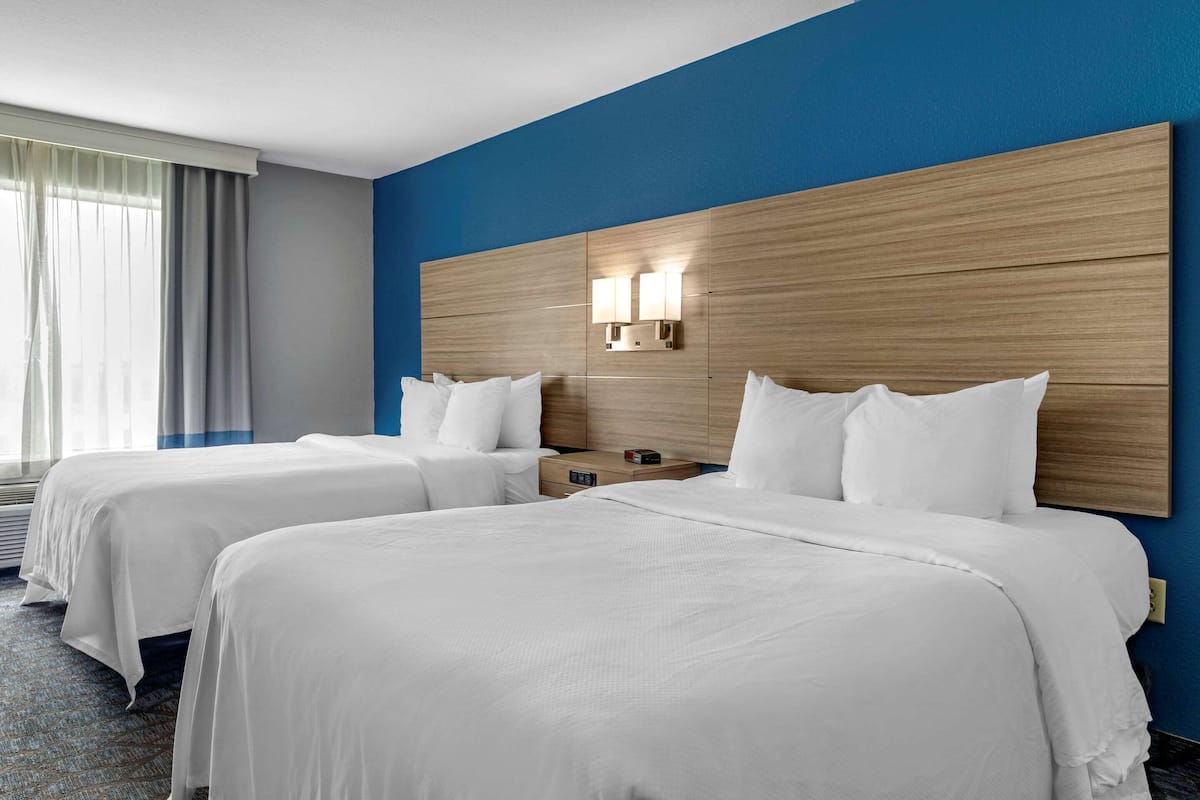 A hotel room with two beds, a wooden headboard, a nightstand, and a window with curtains.