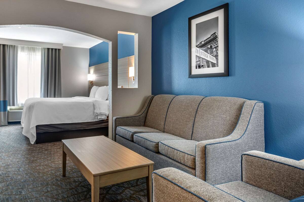A hotel room with a bed, a sofa, a coffee table, and a framed picture on the wall.