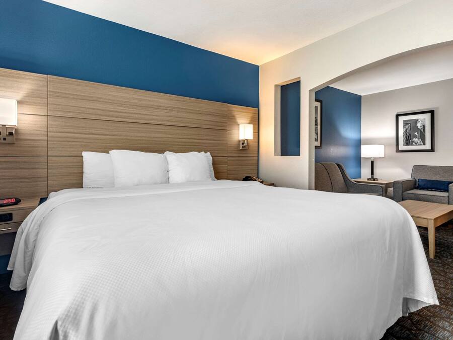 A hotel room with a large bed, a desk, and a chair. There is a nightstand with a lamp and a clock.