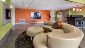 Un hall d’hôtel avec un canapé d’angle, un téléviseur à écran plat et un comptoir de réception.