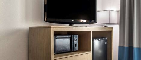 A hotel room with a flat-screen TV on a wooden cabinet, a microwave, and a mini-fridge.