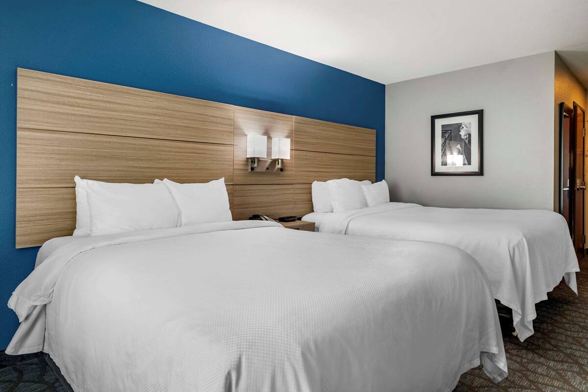 A hotel room with two beds, a wooden headboard, a nightstand with a phone, and a framed picture on the wall.