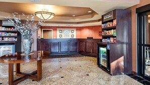 A hotel lobby with a reception desk, a vase with flowers, a refrigerator, and a snack bar. - Comfort Suites Dulles Airport (Chantilly)