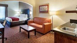 A hotel room with a bed, a sofa, a coffee table, a desk, and a kitchenette. - Comfort Suites Dulles Airport (Chantilly)