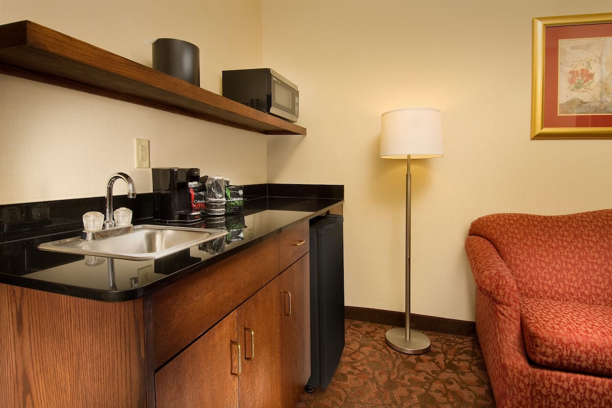 Ein Hotelzimmer mit Küchenzeile, inklusive Spüle, Mikrowelle und Kaffeemaschine. Im Raum befinden sich ein Sofa und eine Lampe.