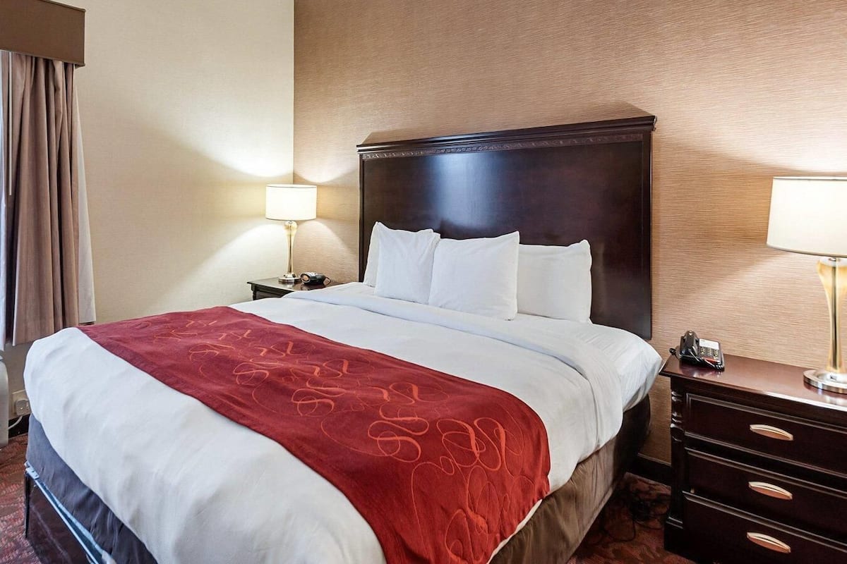 Ein Hotelzimmer mit einem großen Bett, zwei Nachttischen, einem Holzkopfteil und einer roten Tagesdecke.