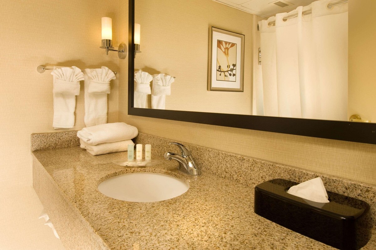 A bathroom with a granite countertop, a white sink, a black tissue box, and a framed artwork on the wall.