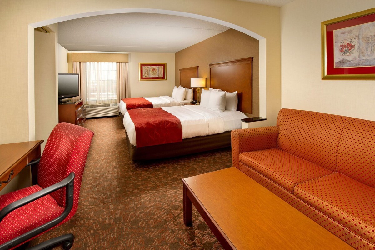 A hotel room with two beds, a sofa, a desk, and a chair.