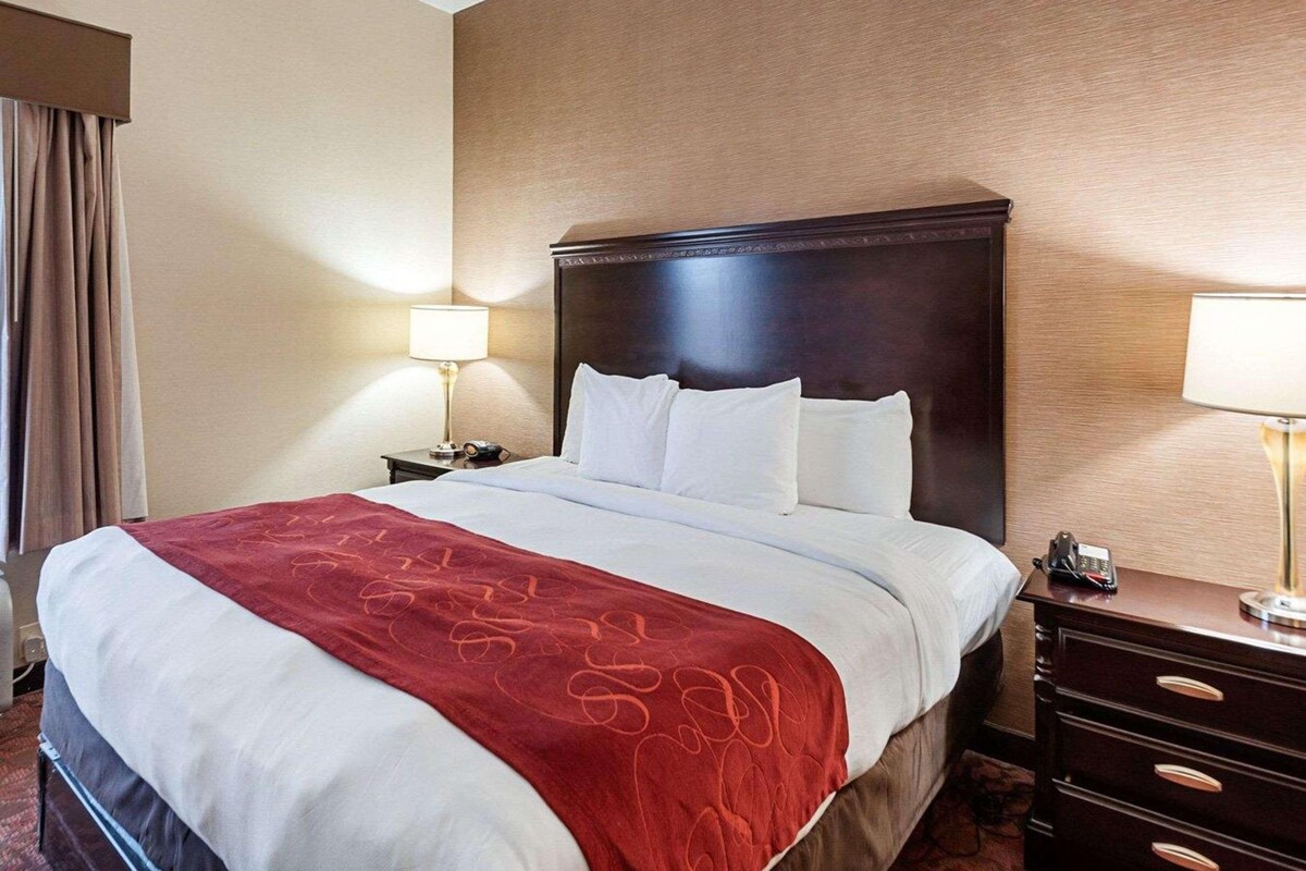 A hotel room with a large bed, two bedside tables, a red throw blanket, and a wooden headboard.
