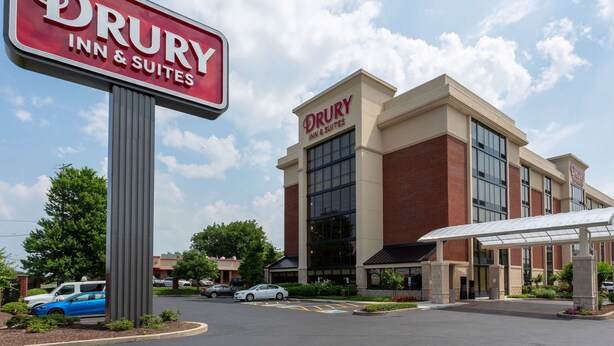A Drury Inn & Suites building with a large sign, a covered entrance, and a parking lot with cars.