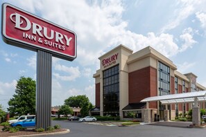 Edificio de Drury Inn & Suites con un letrero grande, entrada cubierta y estacionamiento con coches.