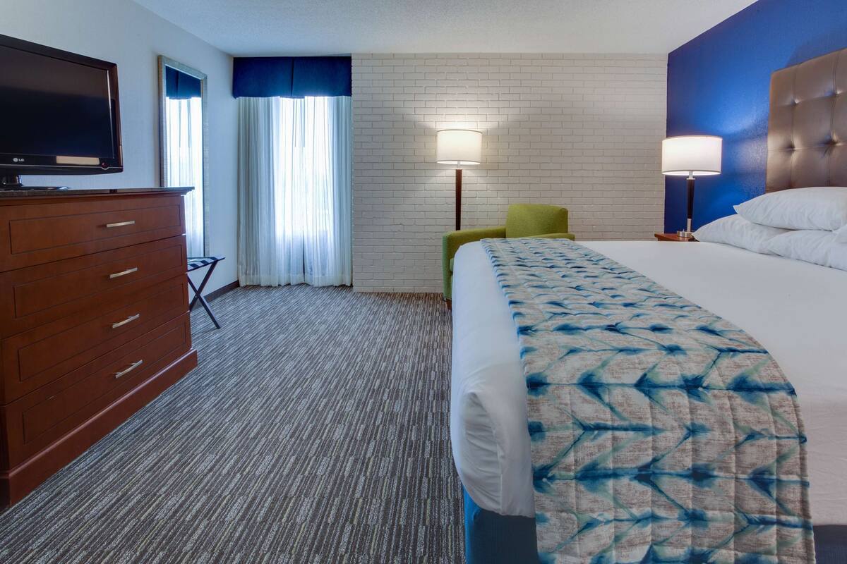 A hotel room with a bed, a TV, a dresser, a lamp, and a chair.