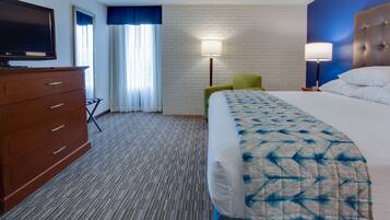 A hotel room with a bed, a television, a dresser, a chair, and a lamp.