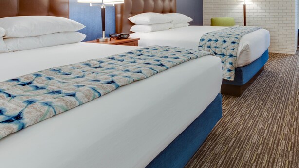 Habitación de hotel con dos camas, cabeceros, lámparas de noche y una pared con diseño de ladrillo.