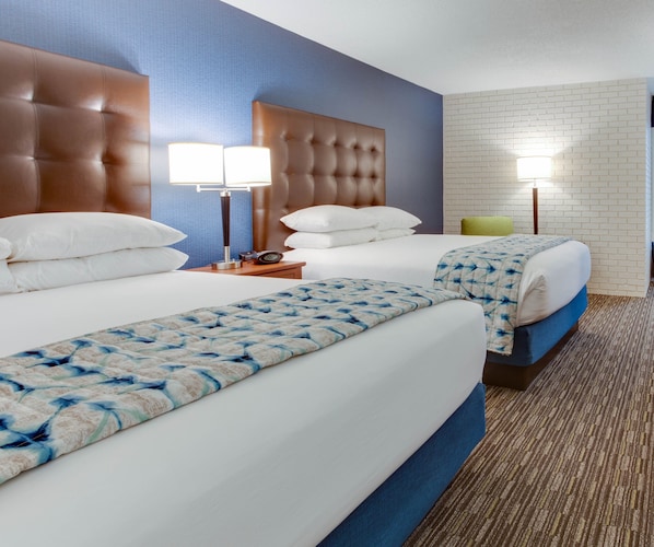 Habitación de hotel con dos camas, cabeceros, lámparas de noche y una pared con diseño de ladrillo.