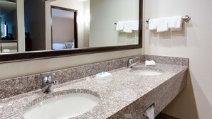 A hotel bathroom with two sinks, a large mirror, and a towel rack with multiple towels.