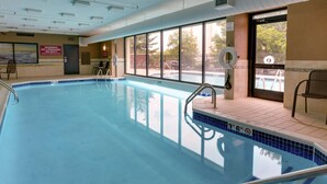 Una piscina interior con señalización de seguridad clara, una silla de socorrista y vistas al exterior.