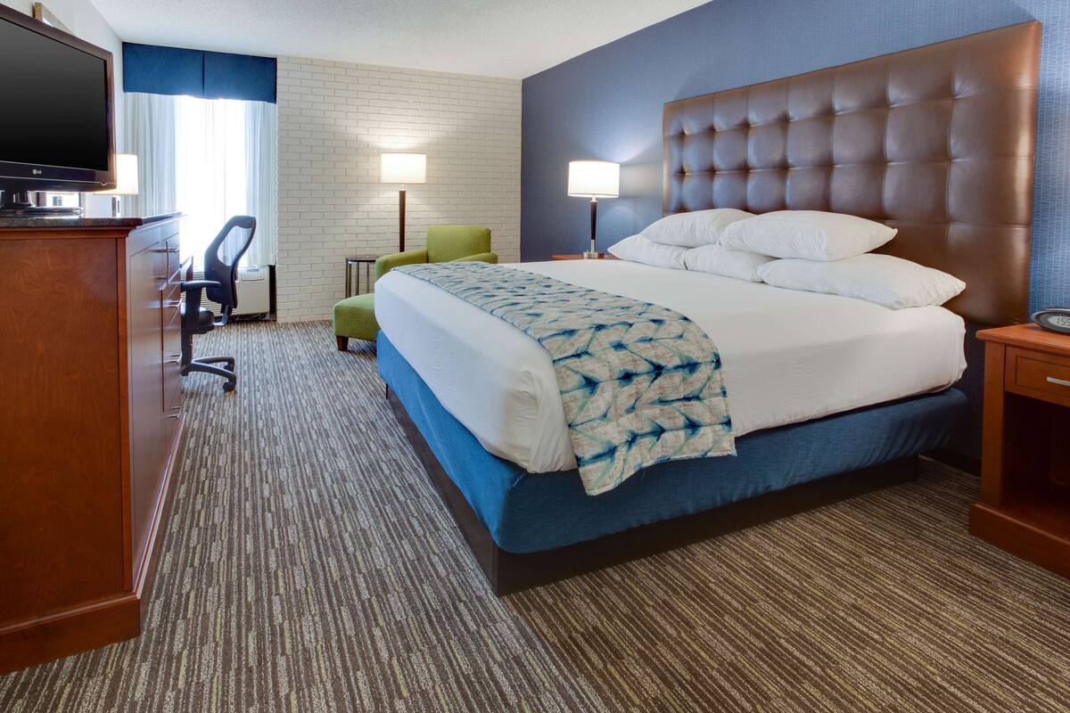 A hotel room with a large bed, a desk with a TV, a chair, and two lamps.