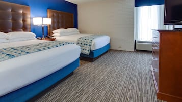 A hotel room with two beds, a television, and a brick wall.