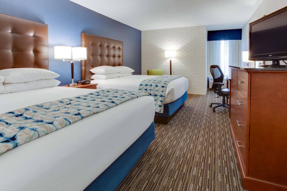 A hotel room with two beds, a television, a desk, and a chair.