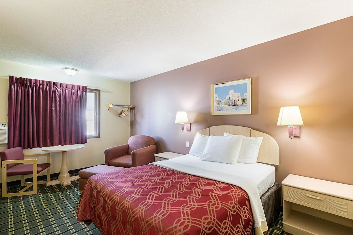 A hotel room with a bed, two chairs, a small table, and a painting on the wall.