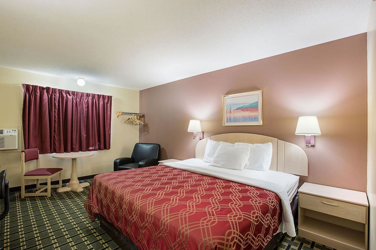A hotel room with a bed, two bedside lamps, a chair, a small table, and a painting on the wall.