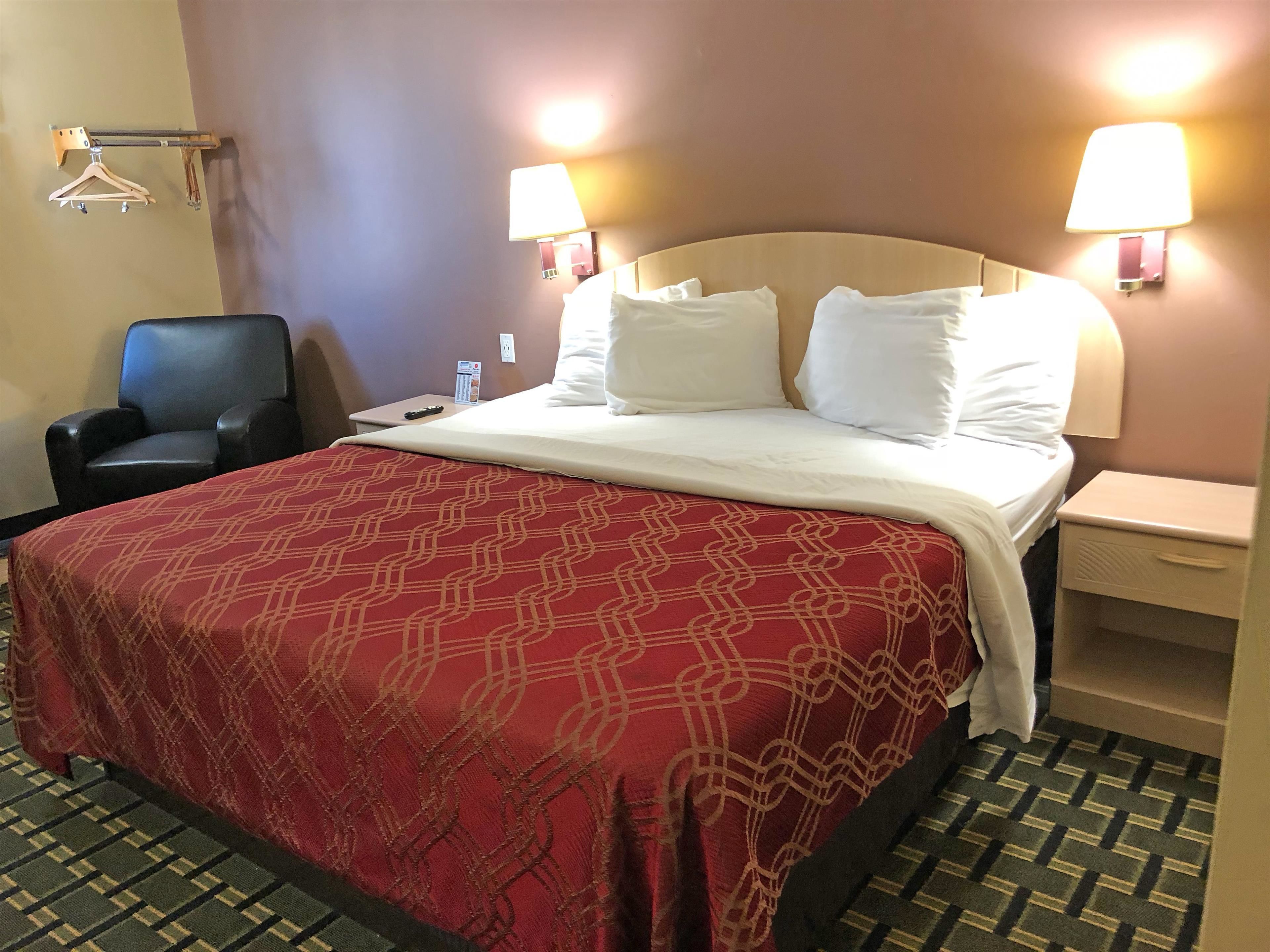 A hotel room with a large bed, two bedside lamps, a chair, a nightstand, and a wall-mounted lamp.
