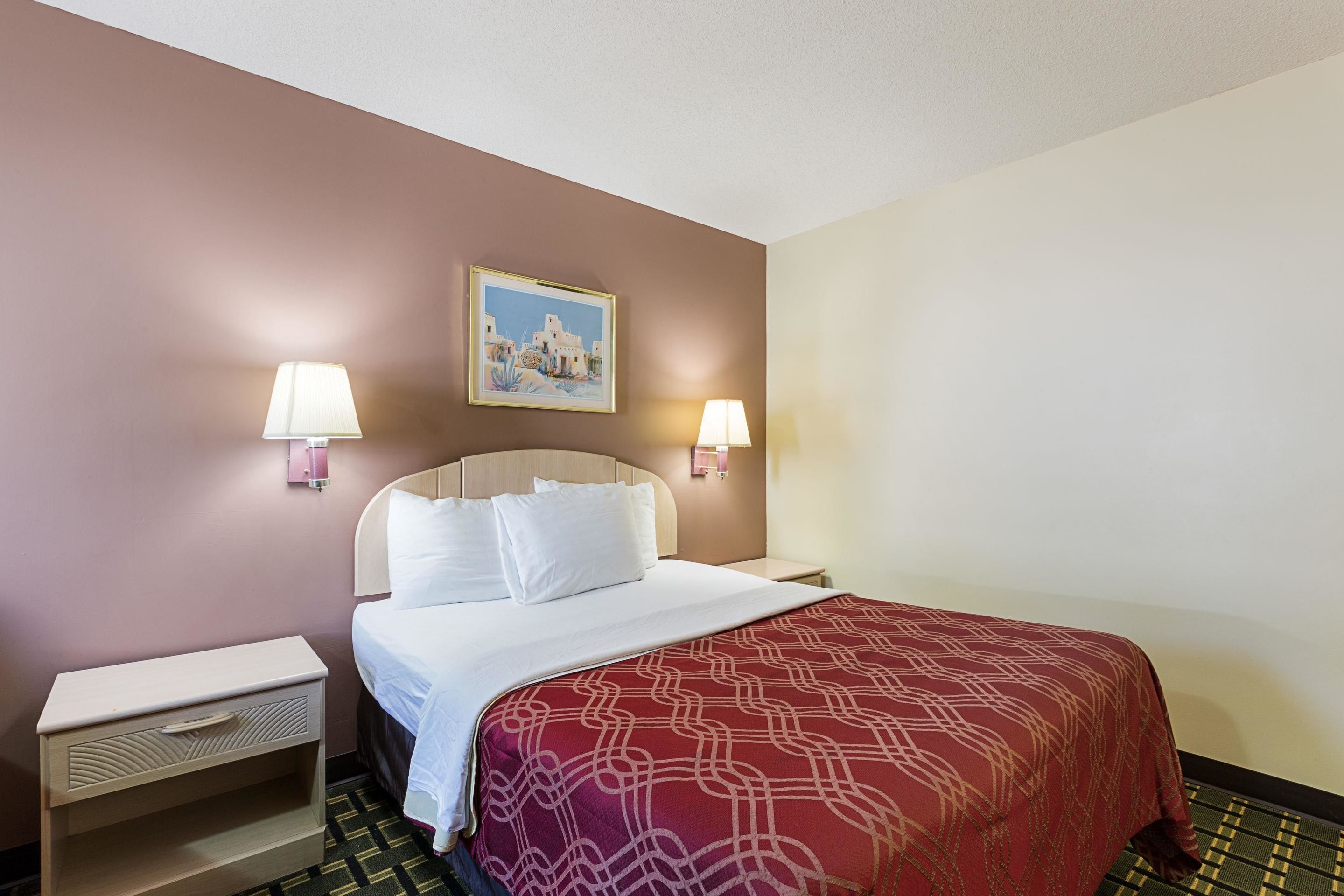 Habitación de hotel con cama, dos lámparas de noche, una mesita de noche, un cuadro en la pared y una colcha estampada.