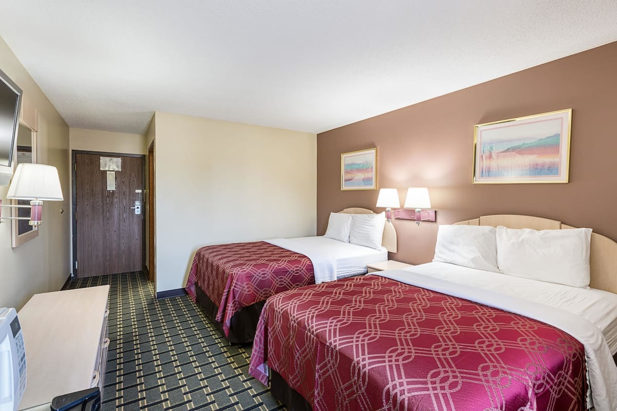 A hotel room with two beds, a desk, a chair, a lamp, and a door.