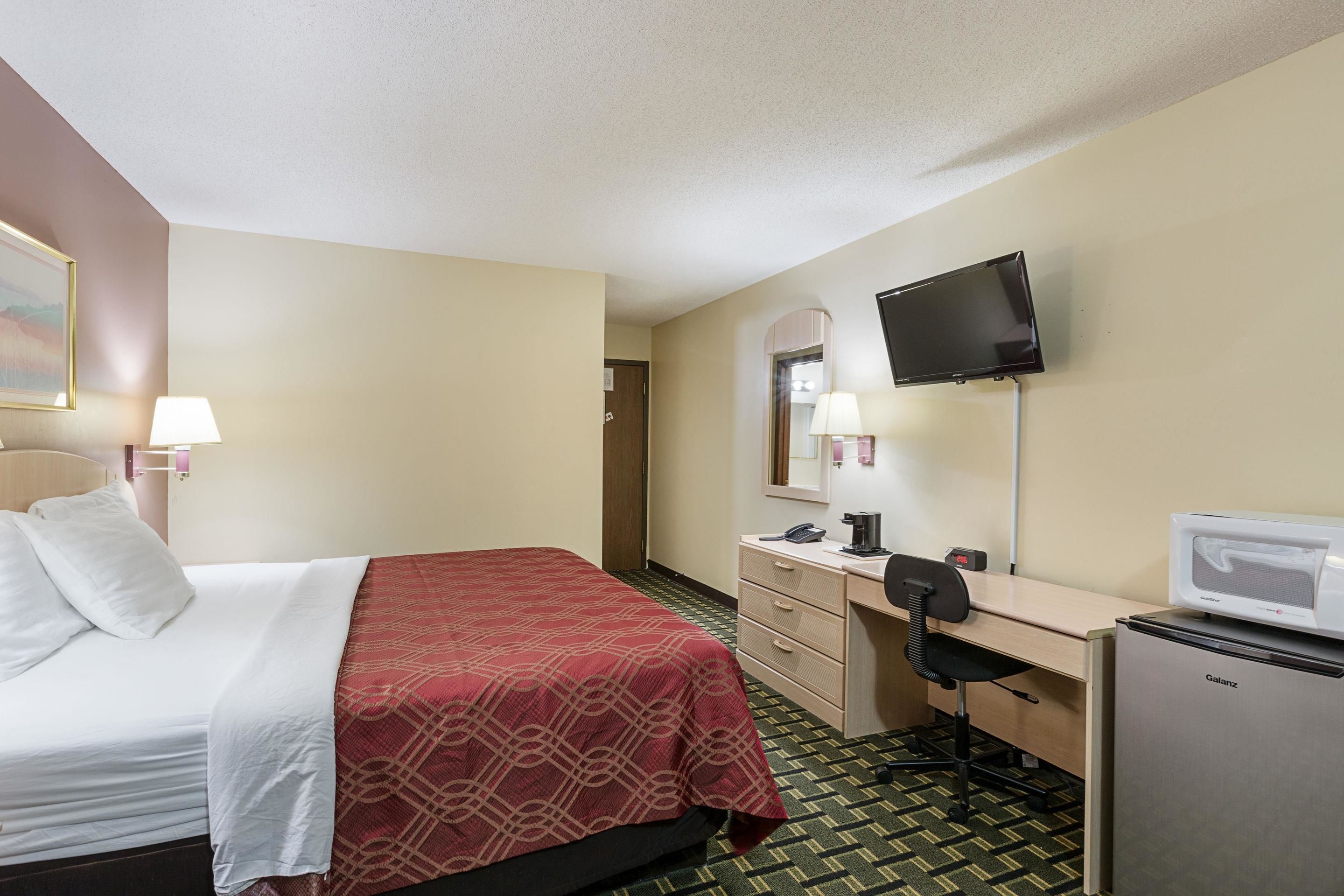 Habitación de hotel con cama, escritorio, silla, televisor y refrigerador.