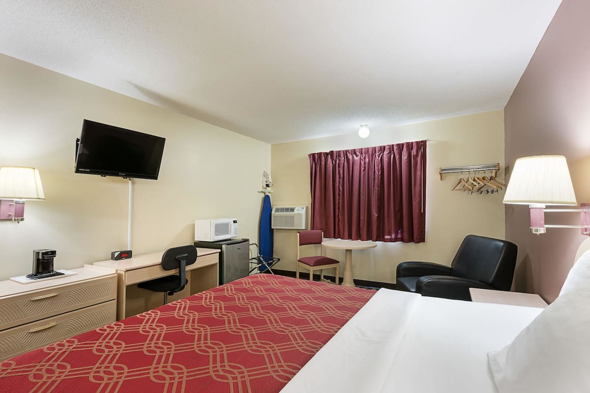 A hotel room with a bed, desk, chair, TV, and a small table with a lamp.