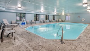 Une piscine intérieure à l’eau claire, entourée de chaises longues et dotée d’un sol carrelé.