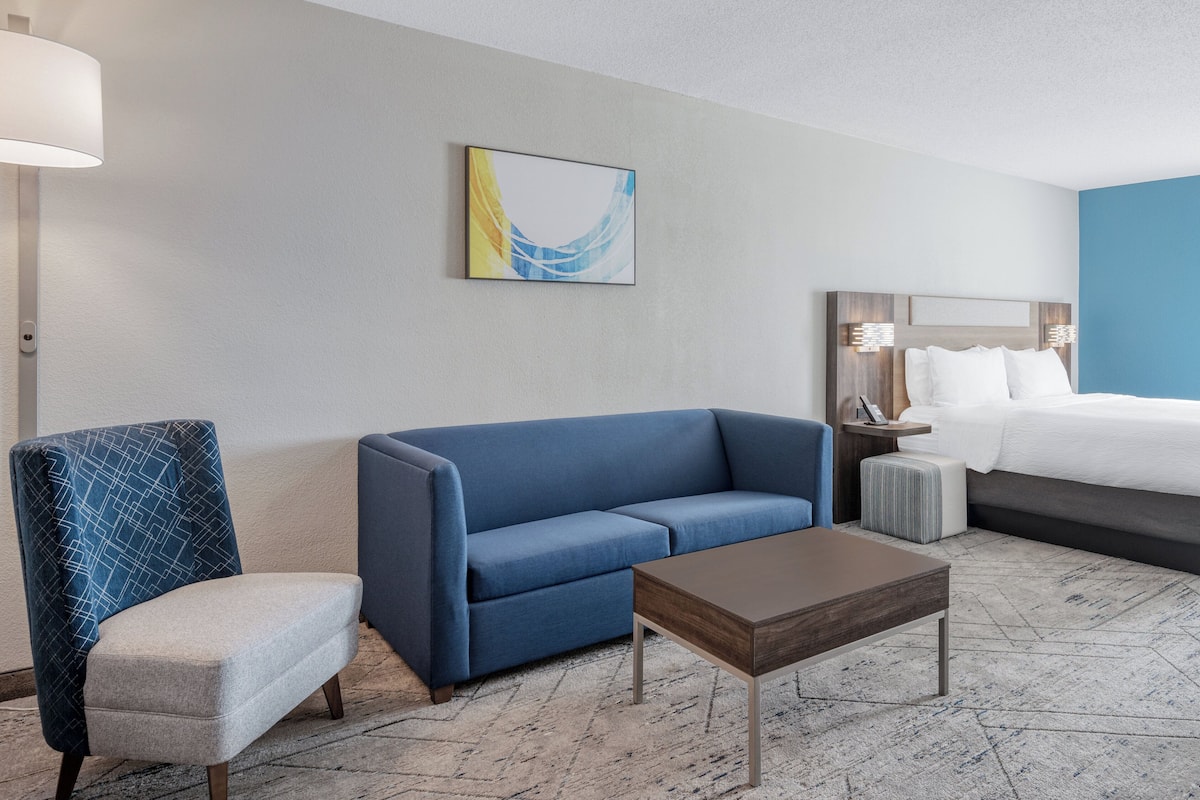 Ein Hotelzimmer mit einem blauen Sofa, einem kleinen Tisch, einem Sessel, einem Bett und einem Wandbild.