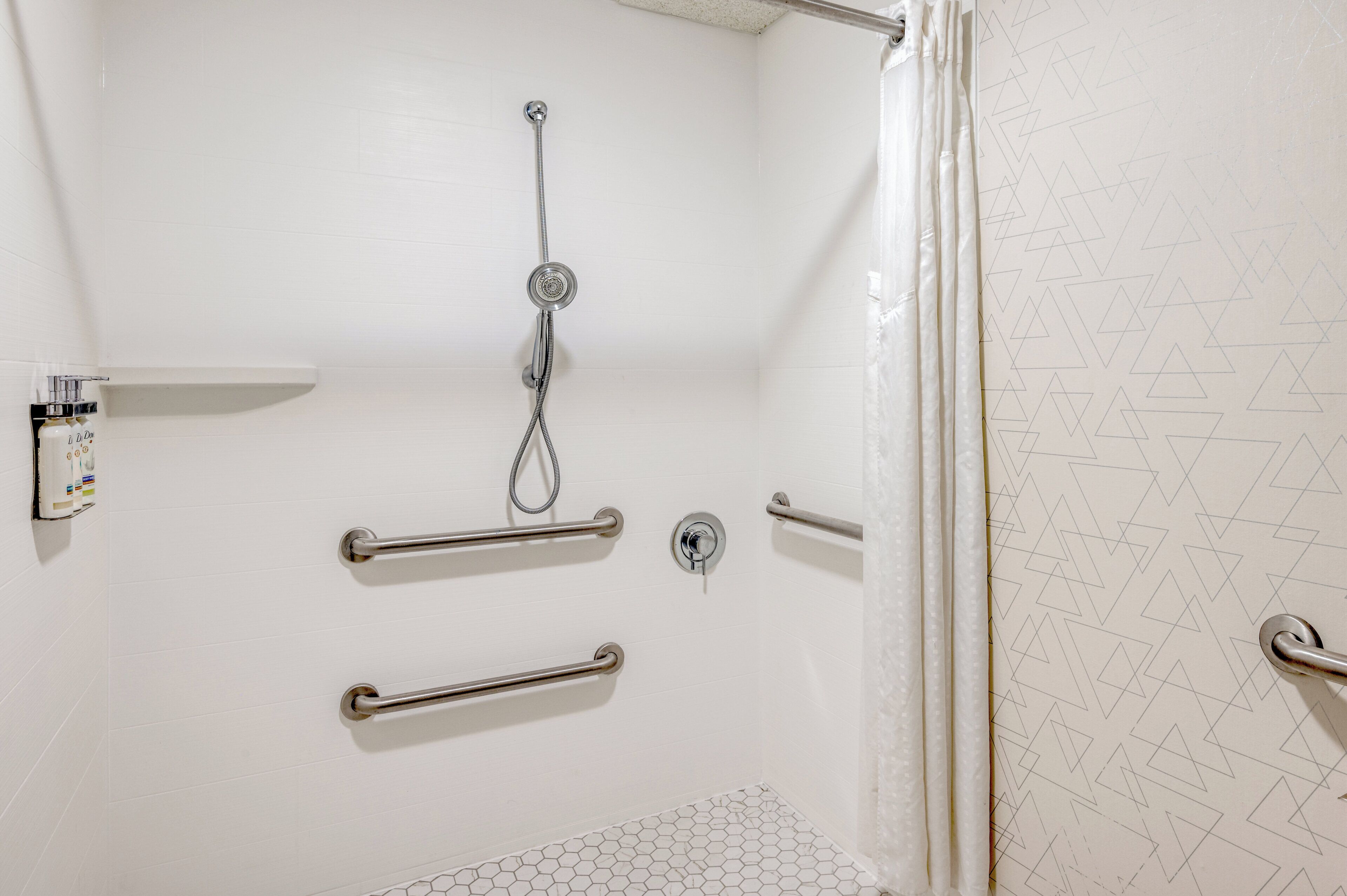 A bathroom with a shower, grab bars, and a toilet.