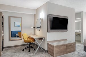 Una habitación de hotel con escritorio, silla, televisor y espejo.