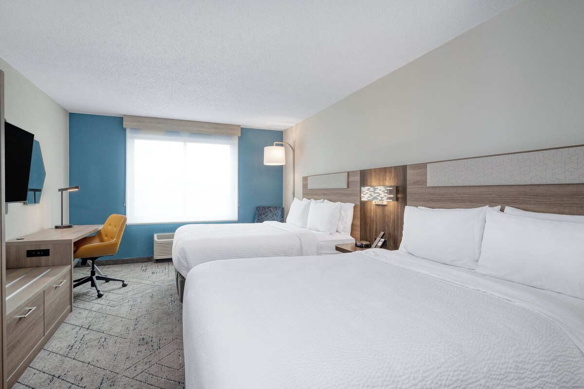 Habitación de hotel con dos camas, un escritorio, una silla de oficina y un ventanal grande.