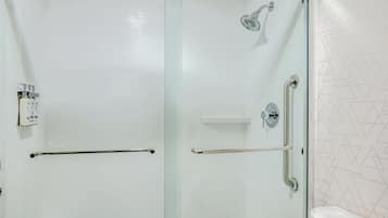 A modern bathroom with a glass shower enclosure, a handrail, and a toilet.