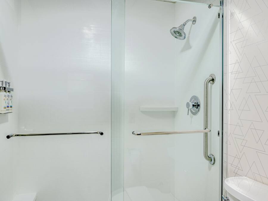 Une salle de bain moderne dotée d’une douche à parois de verre, d’une barre d’appui et de toilettes.