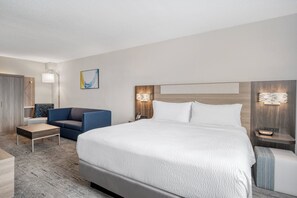 Een moderne hotelkamer met een groot bed, een blauwe fauteuil, een kleine tafel en een nachtkastje met een lamp.