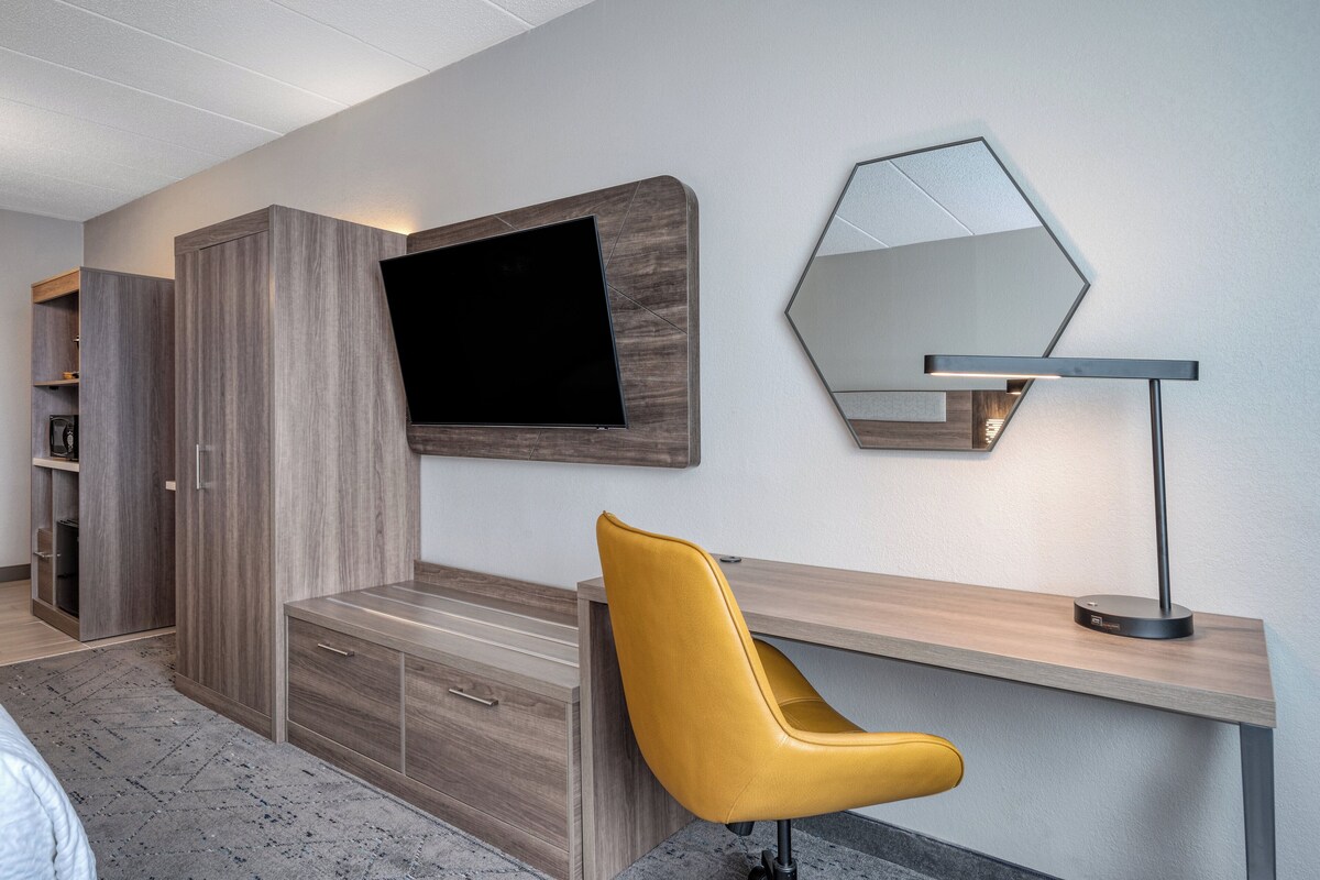 Una habitación moderna con un escritorio de madera, una silla amarilla, un televisor de pantalla plana y un espejo.