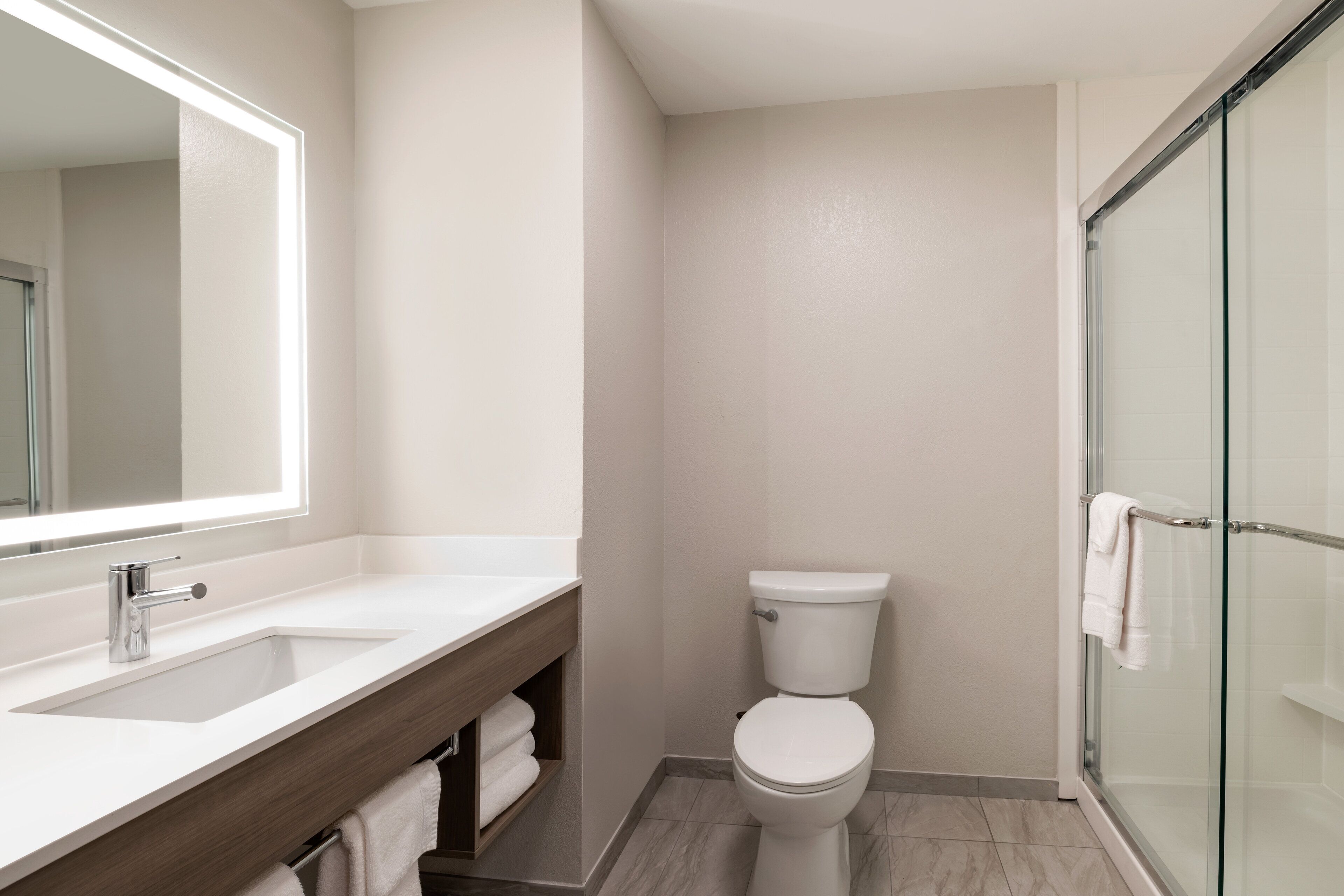 A modern bathroom with a sink, mirror, toilet, and glass shower enclosure.