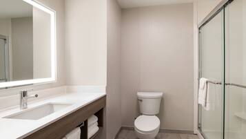 A modern bathroom with a sink, mirror, toilet, and glass shower enclosure.