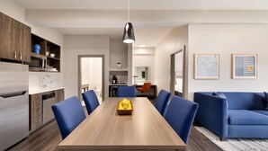 A modern kitchen with a dining area, featuring a wooden table, blue chairs, and a hanging pendant light. - Holiday Inn Express & Suites Opelousas by IHG (Opelousas)