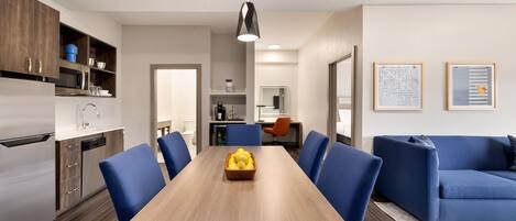 Una cocina moderna con comedor, que presenta una mesa de madera, sillas azules y una lámpara colgante.