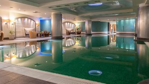 A large indoor swimming pool with a clear water surface, surrounded by lounge areas with seating and tables, and a modern ceiling design. - Regent Warsaw Hotel (Warsaw)
