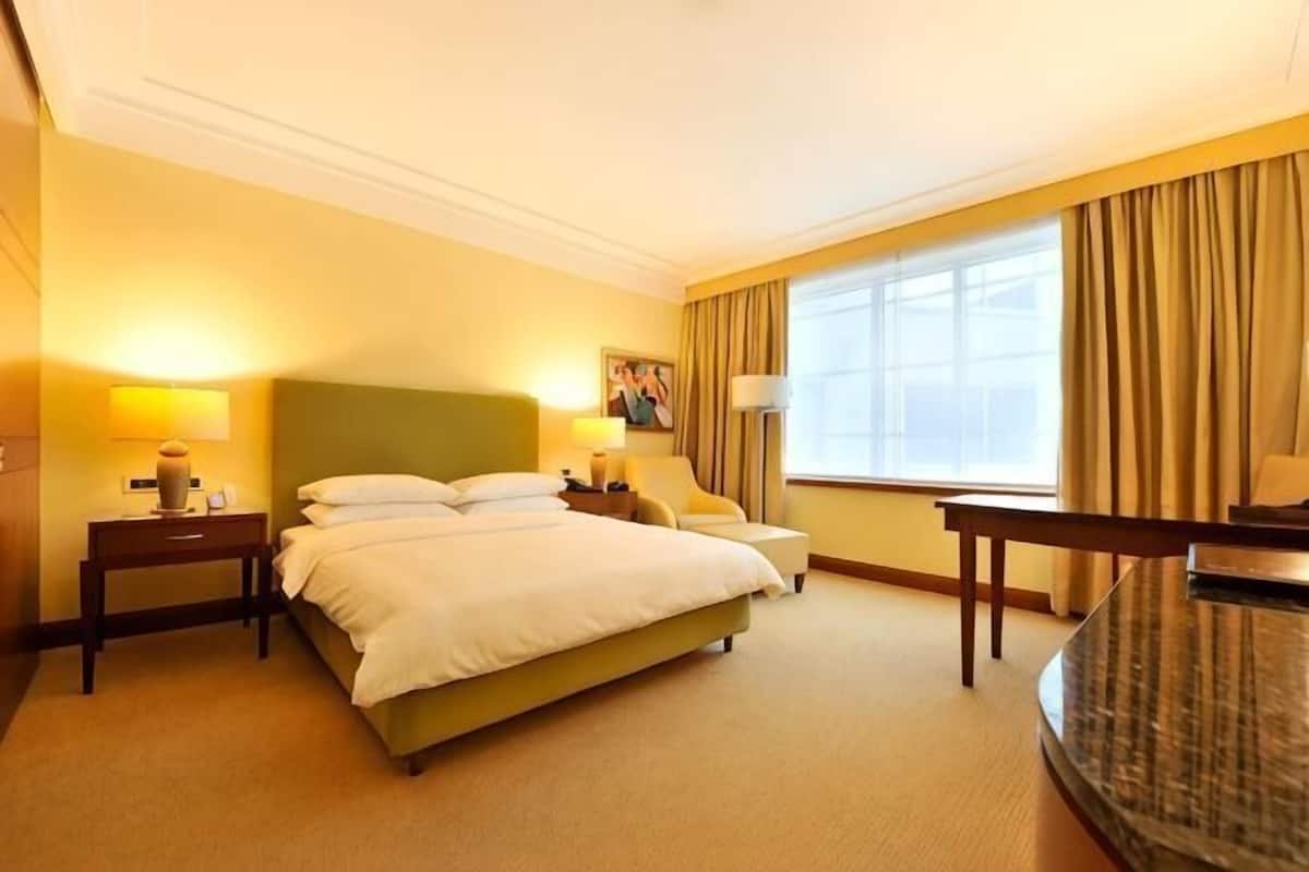A hotel room with a bed, two bedside tables, a desk, a chair, and a window with curtains.